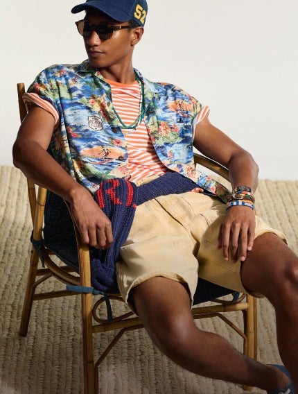 Man in chair wears tropical-print short-sleeve button-down over striped tee and khaki shorts.