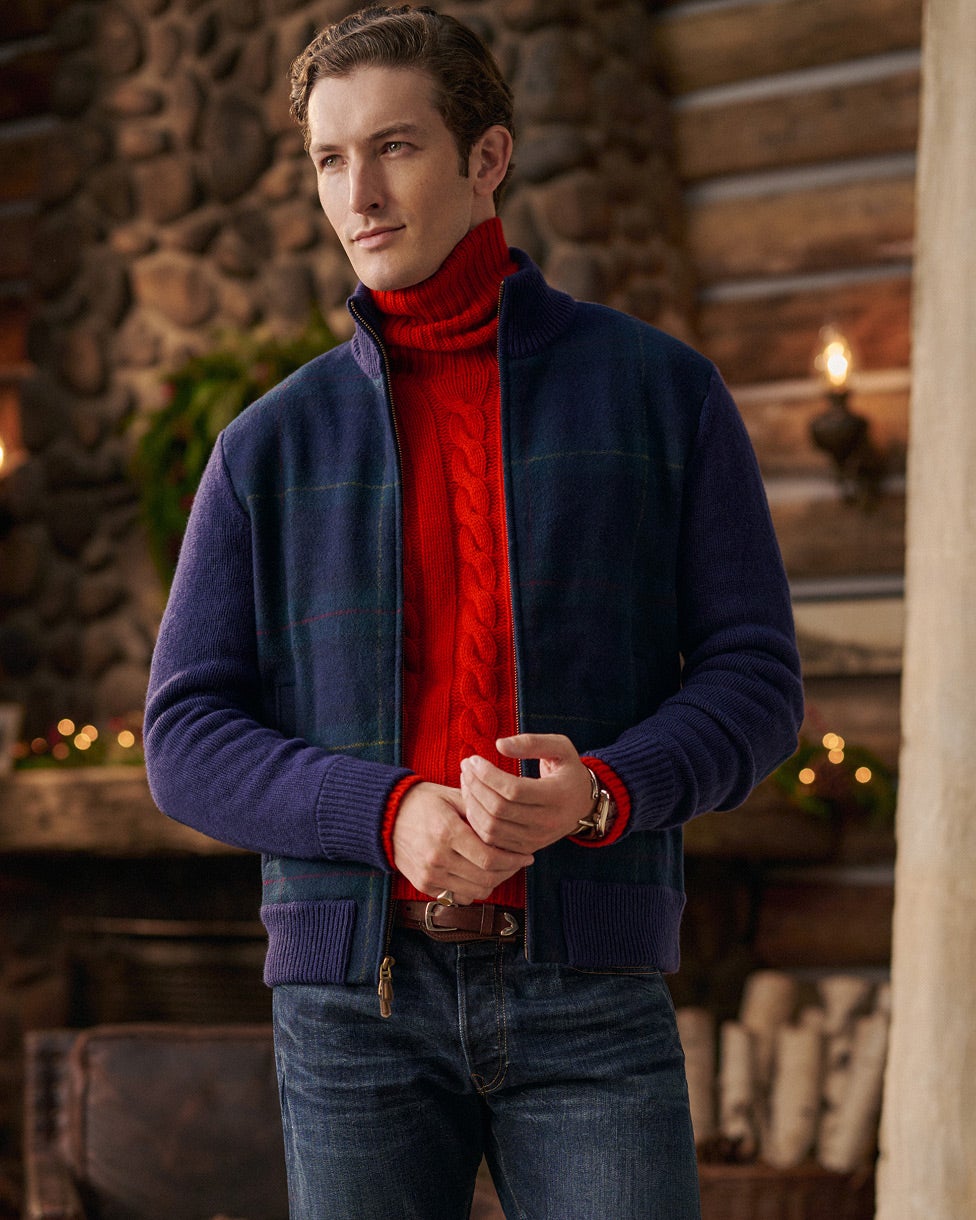 Man wearing a red cable knit turtleneck jumper, navy jacket and jeans.